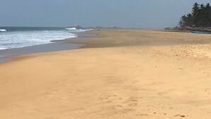 A wide sandy beach with gentle waves, a clear sky, and a line of trees in the distance. - Silence Garden (Hikkaduwa)