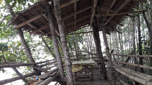 Un pont en bois surmonté d’une structure à toit de chaume, entouré d’un feuillage dense.
