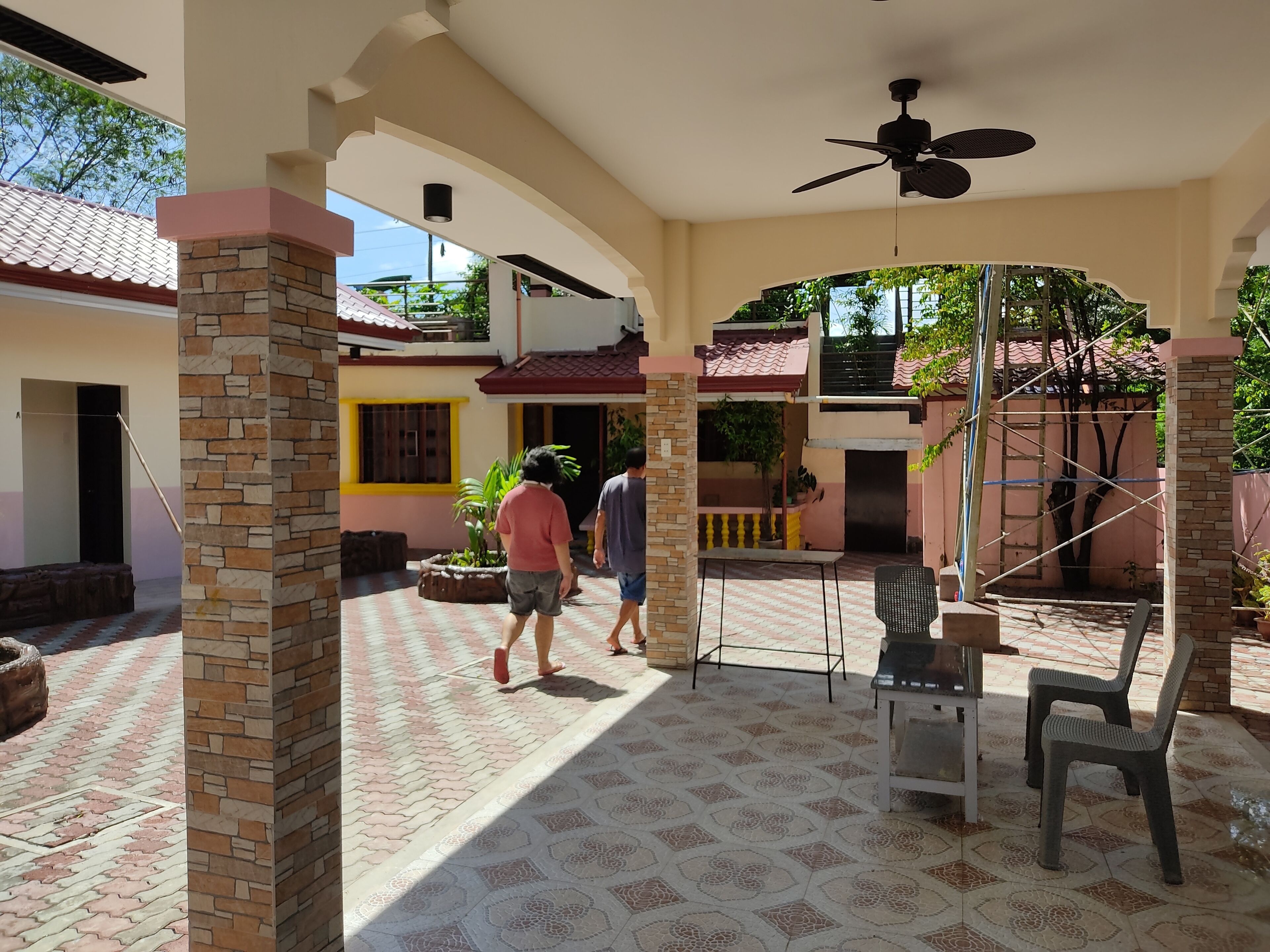 Ein überdachter Patio-Bereich mit Fliesenboden, Deckenventilator und einer Sitzecke mit Stühlen.