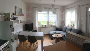 A modern living room with a sofa, a dining table, and a TV. There are windows with curtains and a radiator. - ____To Bachrauschen____Wohlfuelwohnung in the picturesque Ulm valley, 5km to the Lahn valley (Greifenstein-Ulm)