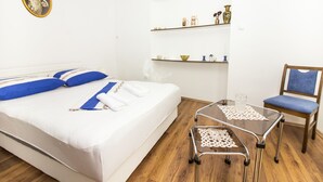 Een netjes opgemaakt bed met blauwe en witte beddengoed, een glazen tafel met een kantbeschermer, een houten stoel met blauwe kussens en een plank met decoratieve objecten.