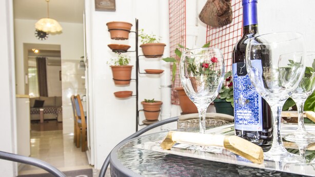 Een ronde glazen tafel met een fles en glazen, omringd door terracotta potten en een rieten stoel.