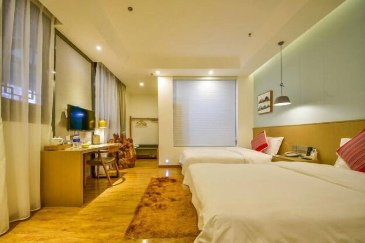 A hotel room with two beds, a desk with a chair, a television, and a window with curtains.