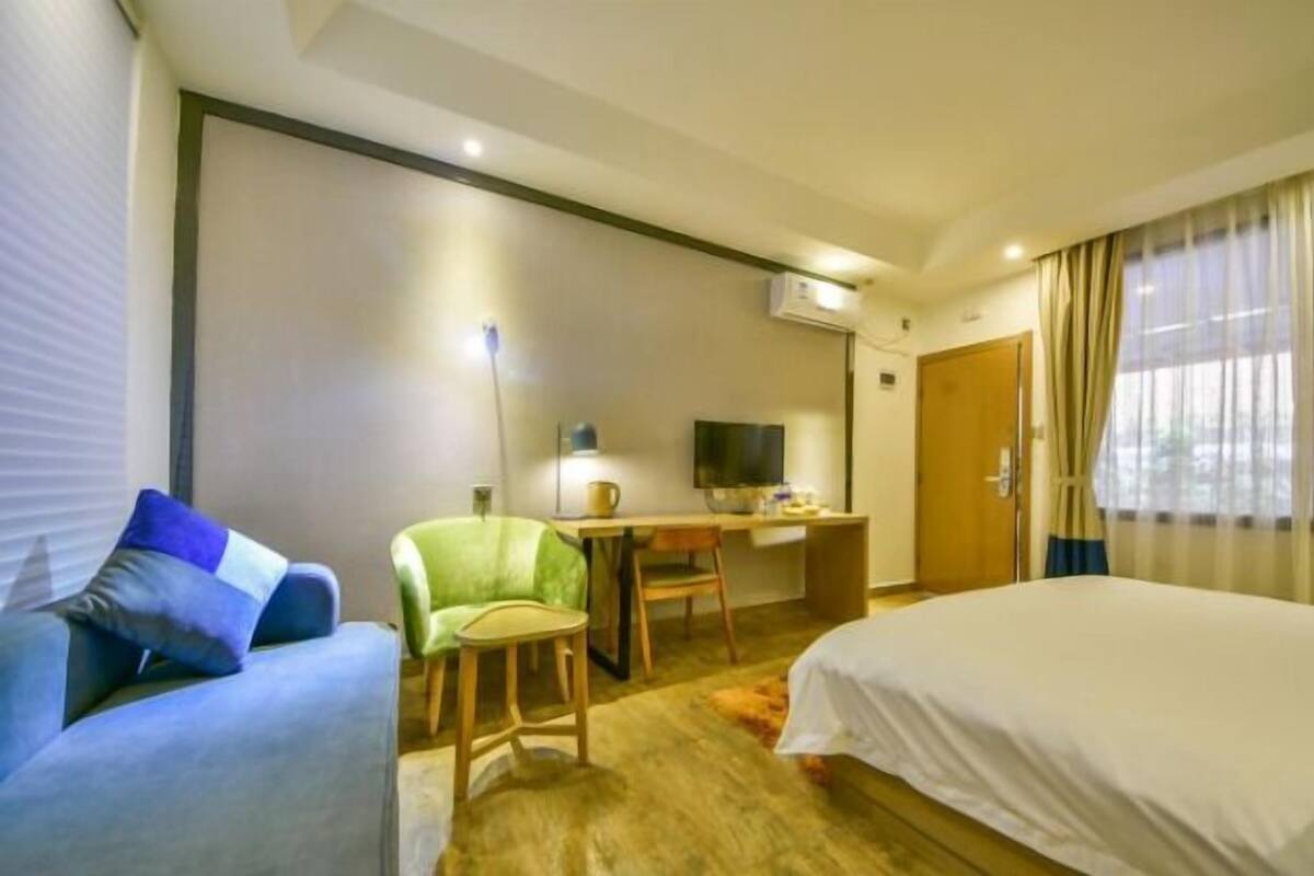 A hotel room with a bed, a desk with a chair, a television, and a window with curtains.