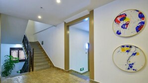 En rymlig hall med en trappa som leder till ett annat våningsplan, en krukväxt och två abstrakta konstverk på väggen.