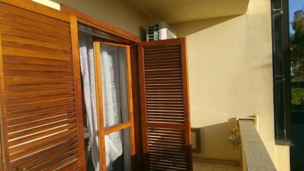 A small balcony with wooden shutters, a tiled floor, and a window with a curtain.