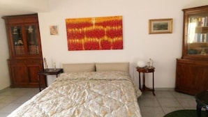 A bedroom with a bed, a wooden cabinet, a small table, and a wall-mounted painting.