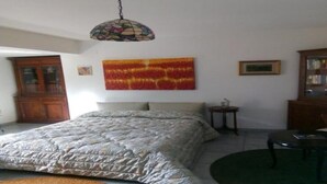 A bedroom with a bed, a small side table, a chair, a wooden cabinet, and a stained glass ceiling light.