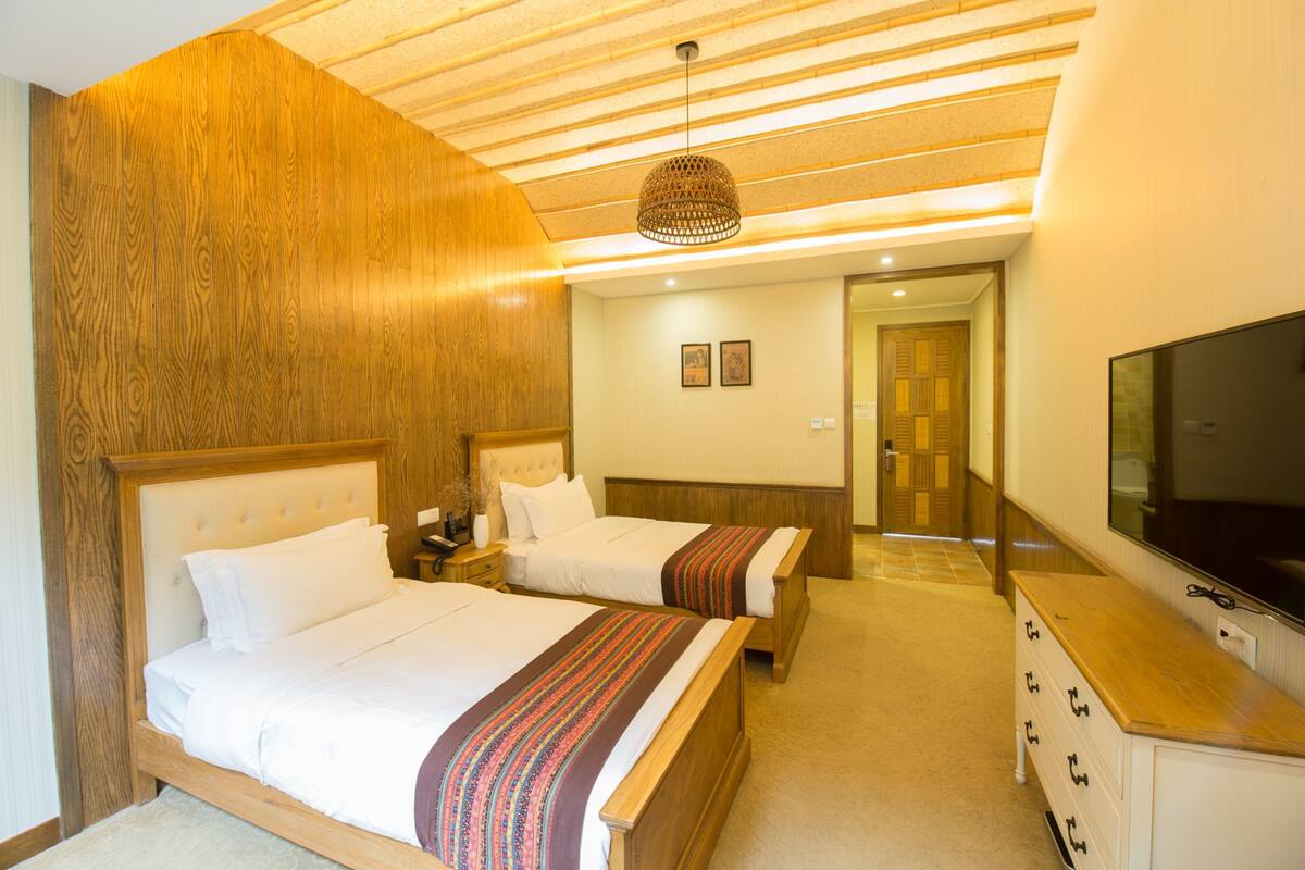 A hotel room with two beds, a TV, a wooden headboard, and a ceiling with wooden slats.