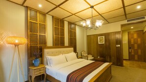 Een hotelkamer met een groot bed, houten lambrisering, een kroonluchter en een nachtkastje met een vaas.