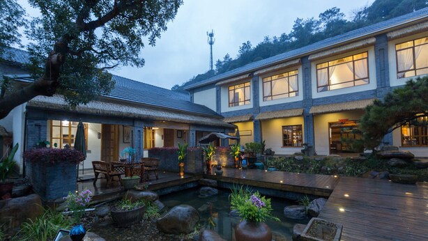Een traditionele Japanse woning met een vijver met koi-karpers, een houten terras en potplanten.