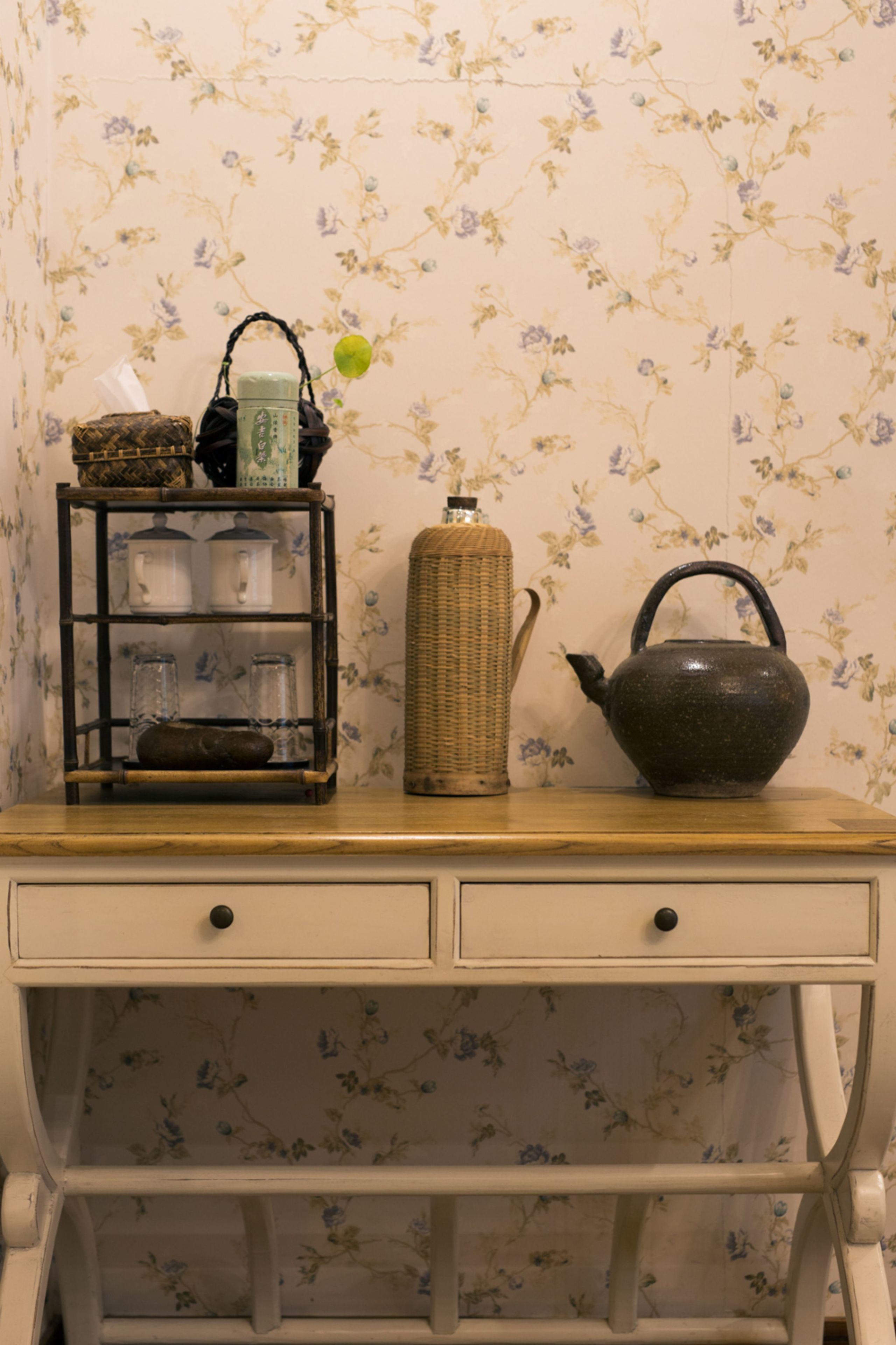 A wooden desk with a woven basket, a teapot, and a small shelf with glass containers.