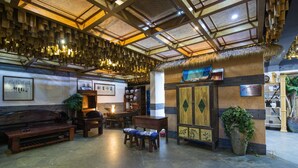 Een ruime lobby met een hoge plafond, houten meubels en een grote potplant.