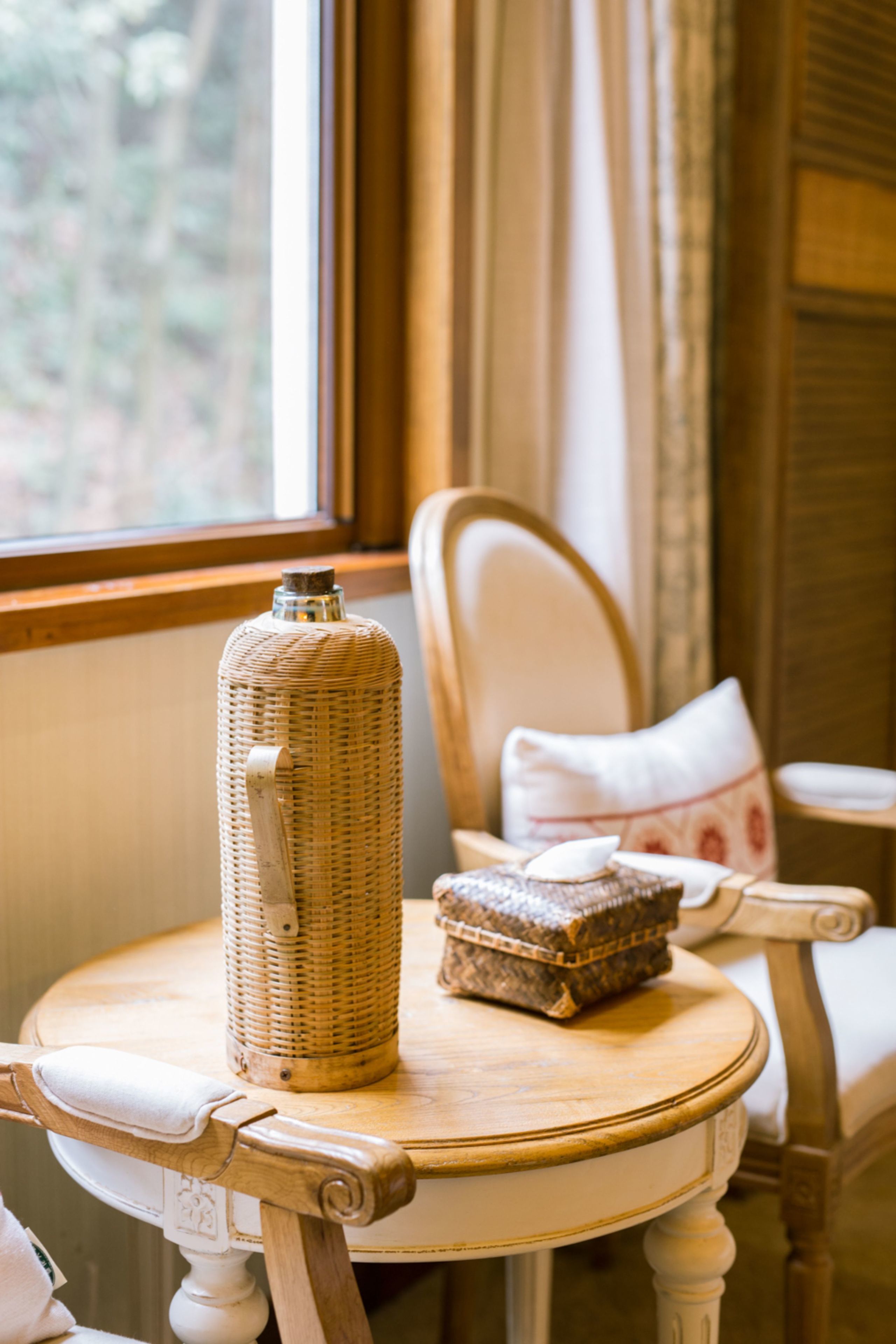 A wicker bottle and a woven basket on a round wooden table.