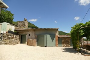 Un bâtiment rustique en pierre, avec une allée de gravier, une porte verte et un petit jardin agrémenté d’une vigne.