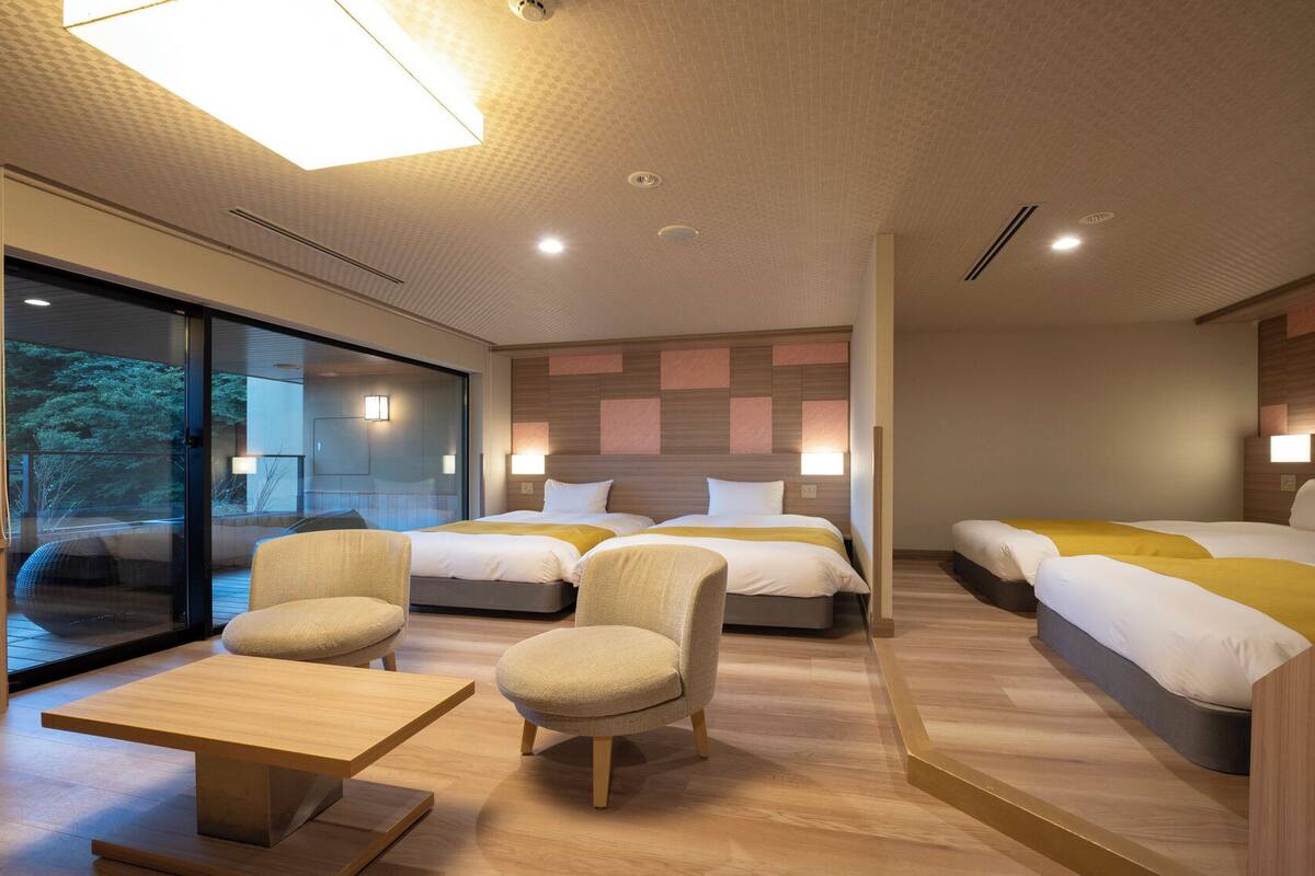 A modern hotel room with two beds, a dining table, and a seating area.