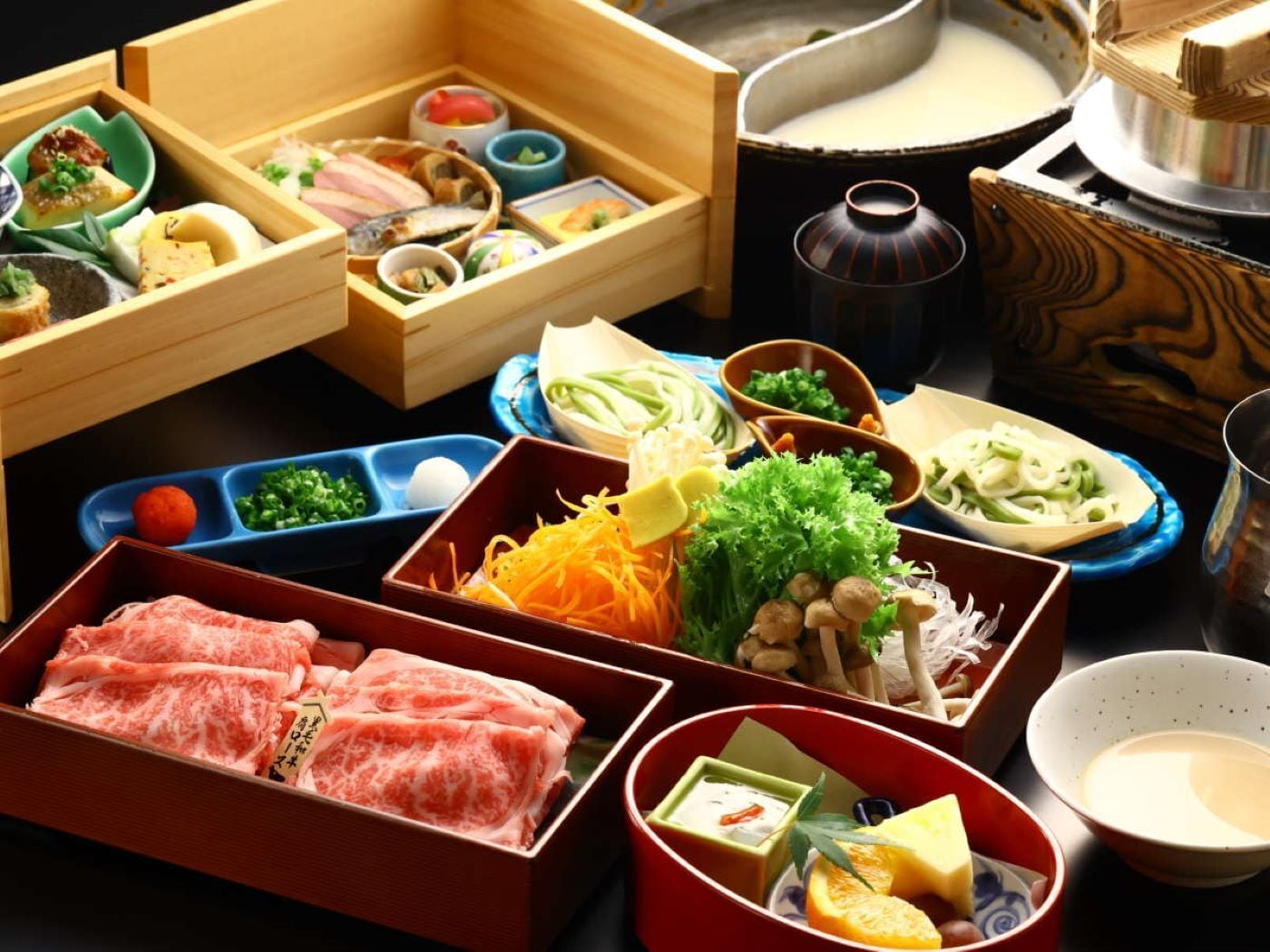 A variety of food items and containers, including a wooden box with sliced meat, a bowl with vegetables, and a pot of soup.