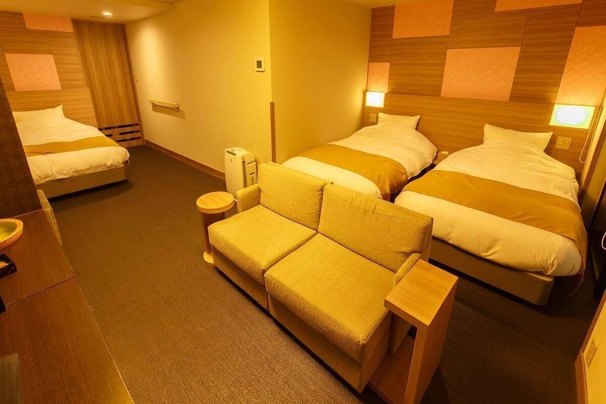 A hotel room with two beds, a sofa, a bedside table, and a lamp.