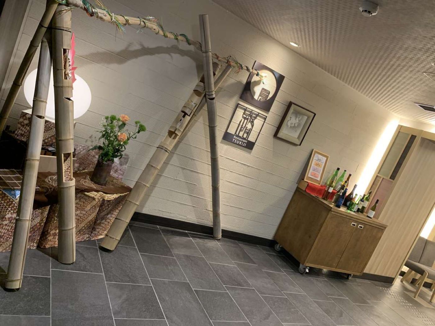 A room with a bamboo structure, a potted plant, a wooden cabinet with bottles, and a wall-mounted sign.