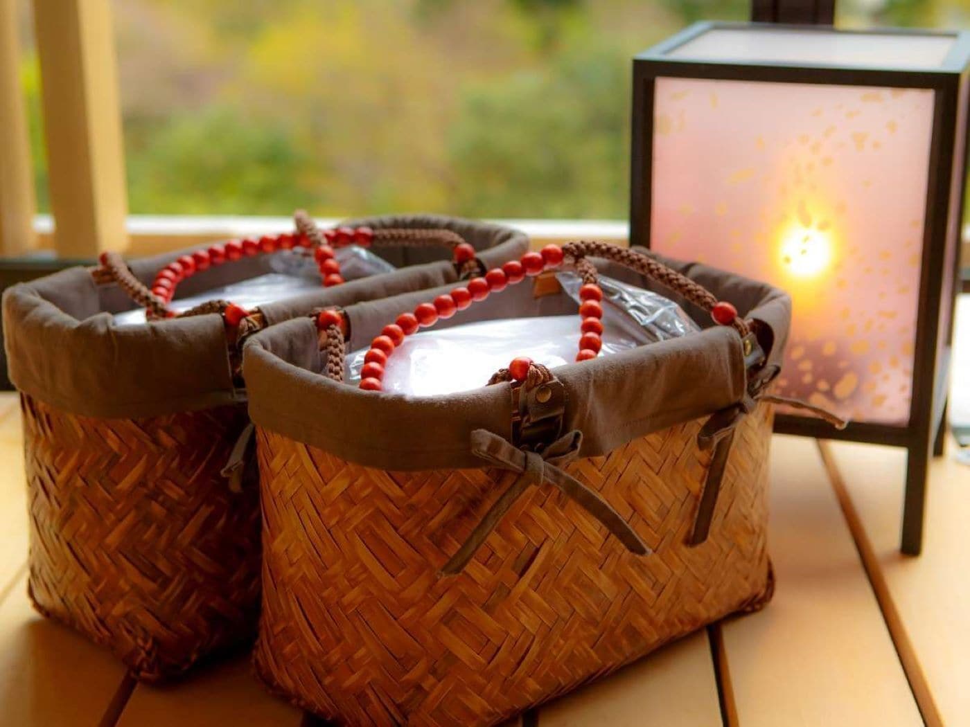 Three woven baskets with handles, placed on a wooden surface next to a lit candle in a glass container.
