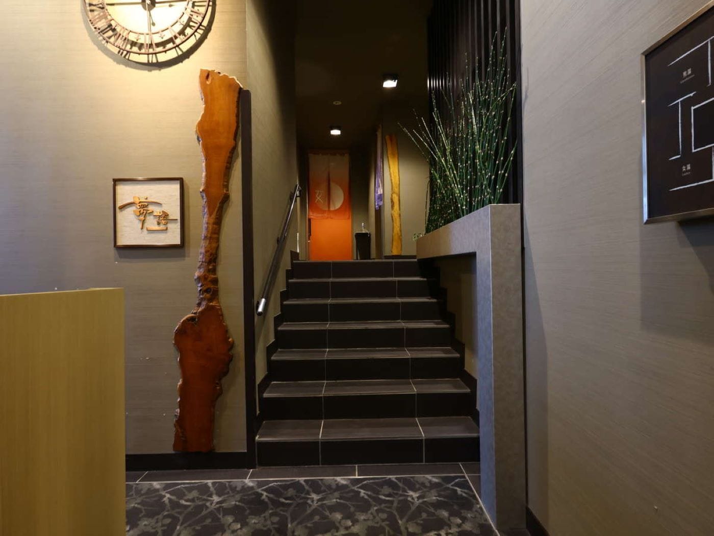 A staircase with a clock on the wall, a framed picture, and a large plant.