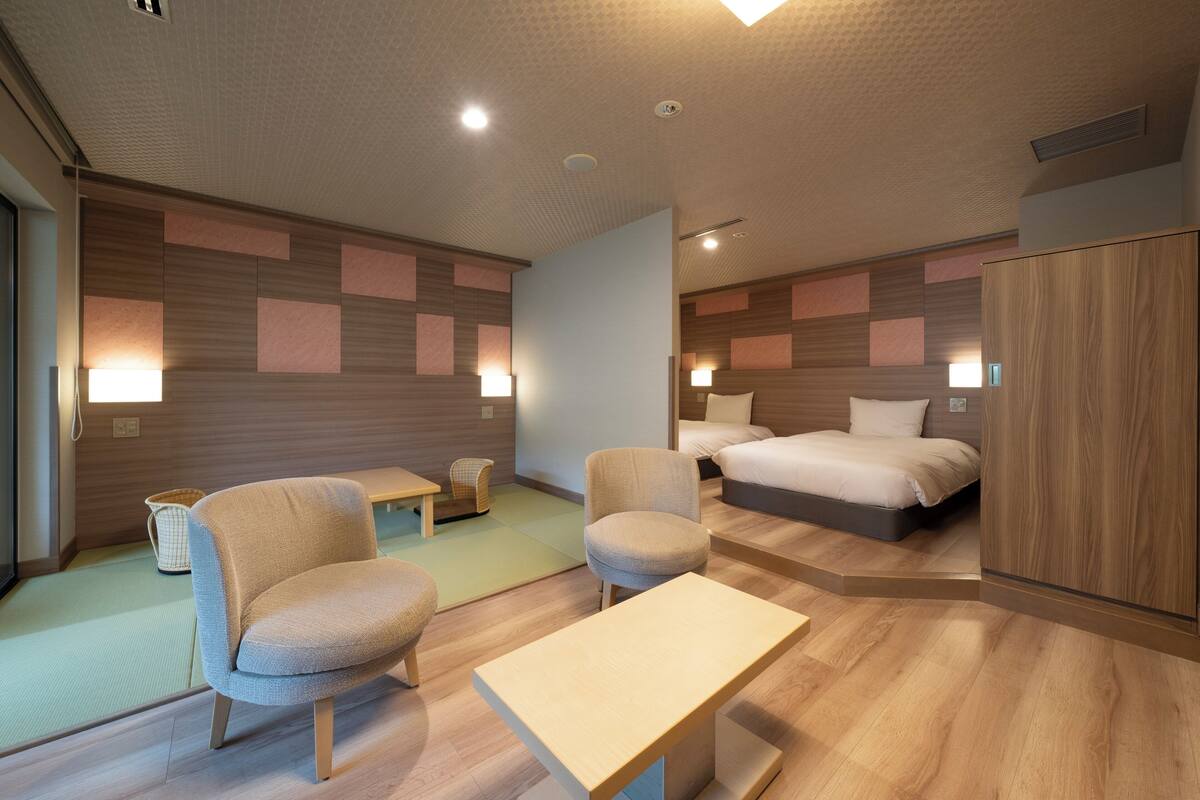 A modern hotel room with a bed, two armchairs, a small table, and a cabinet.