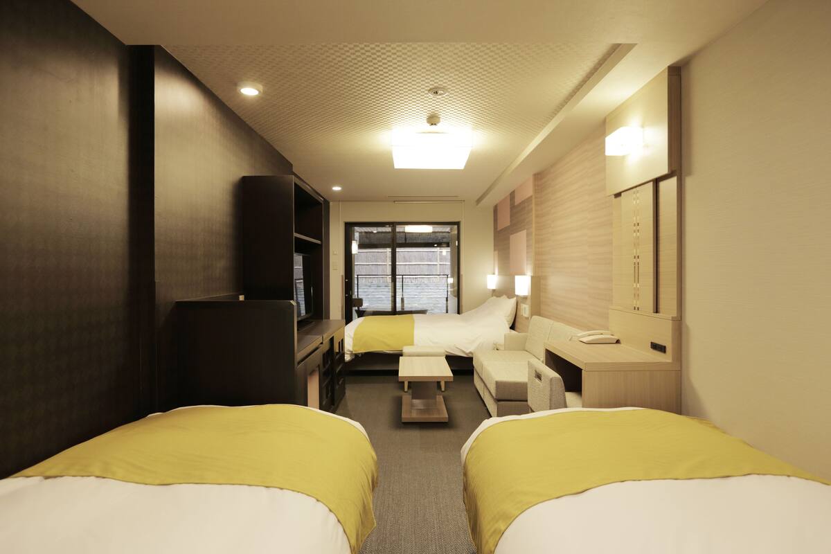 A hotel room with two beds, a desk, a chair, a TV, and a window.