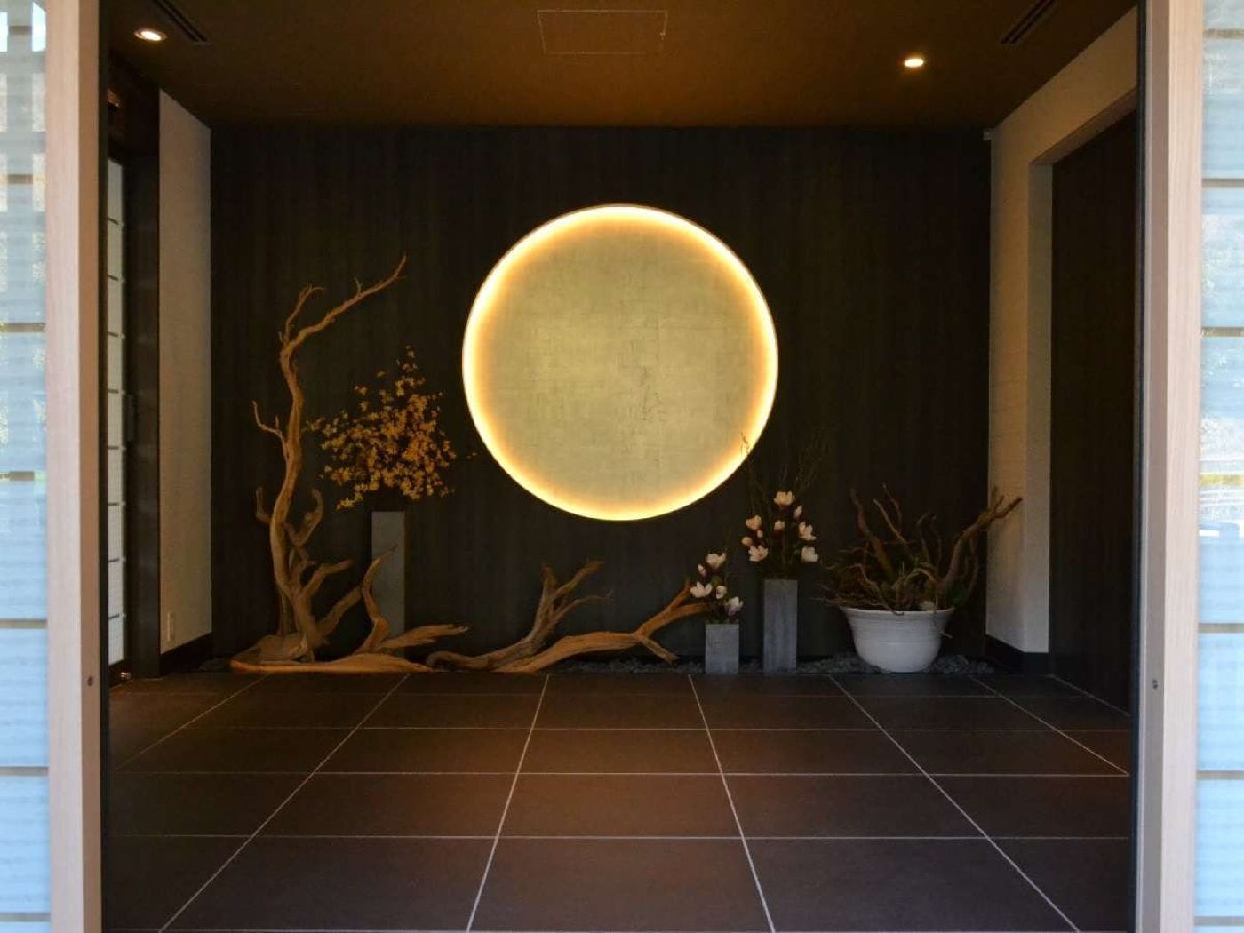A modern interior with a circular illuminated feature on the wall, wooden decor, and tiled flooring.