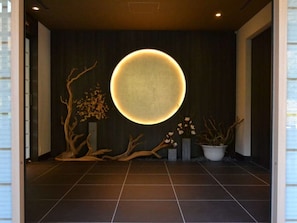A modern interior with a circular illuminated feature on the wall, wooden decor, and tiled flooring. - Tsukino Yado Sara (Hakone)