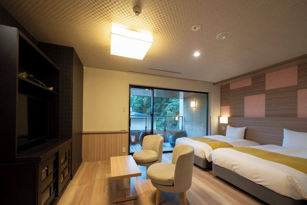 A hotel room with a bed, two chairs, a small table, and a TV.