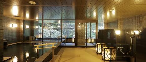 A modern indoor pool area with a wooden ceiling, glass walls, and a view of trees outside.