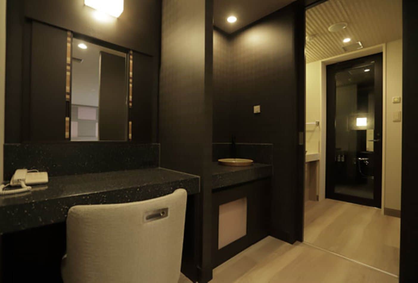 Un bany modern amb taulell fosc, un mirall, un lavabo i una cadira.