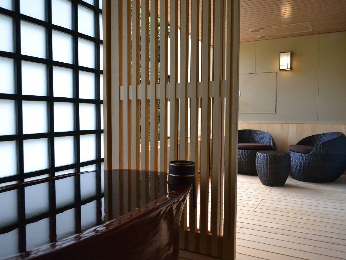 Una habitación con suelo de tatami, una mesa de madera baja y una puerta corredera japonesa tradicional. Hay dos sillas de mimbre oscuro y una pequeña mesa con una vela.