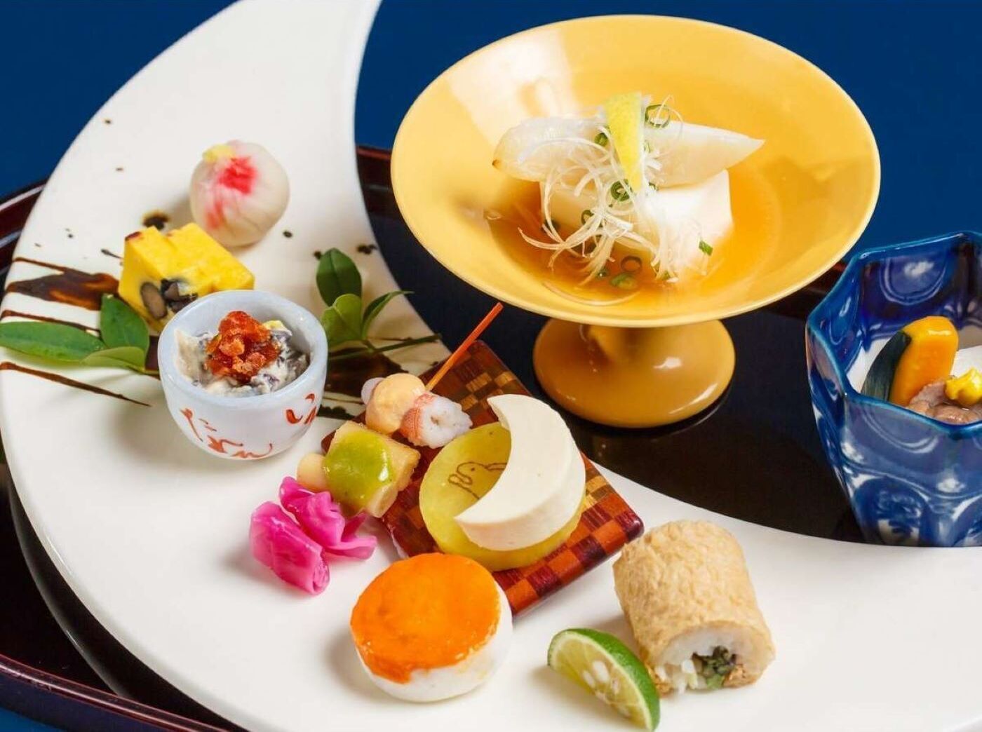 Eine Auswahl an Gerichten auf einem weißen Teller, darunter eine Suppenschüssel, Sushi und weitere kleine Teller mit verschiedenen Speisen.