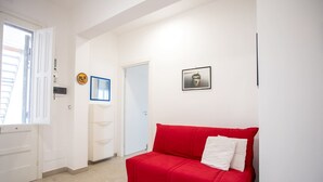 A room with a red sofa, a white door, a framed picture on the wall, and a window with blinds.