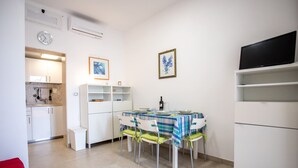 A compact kitchen with white cabinets, a dining table set for four, and a TV on a stand.