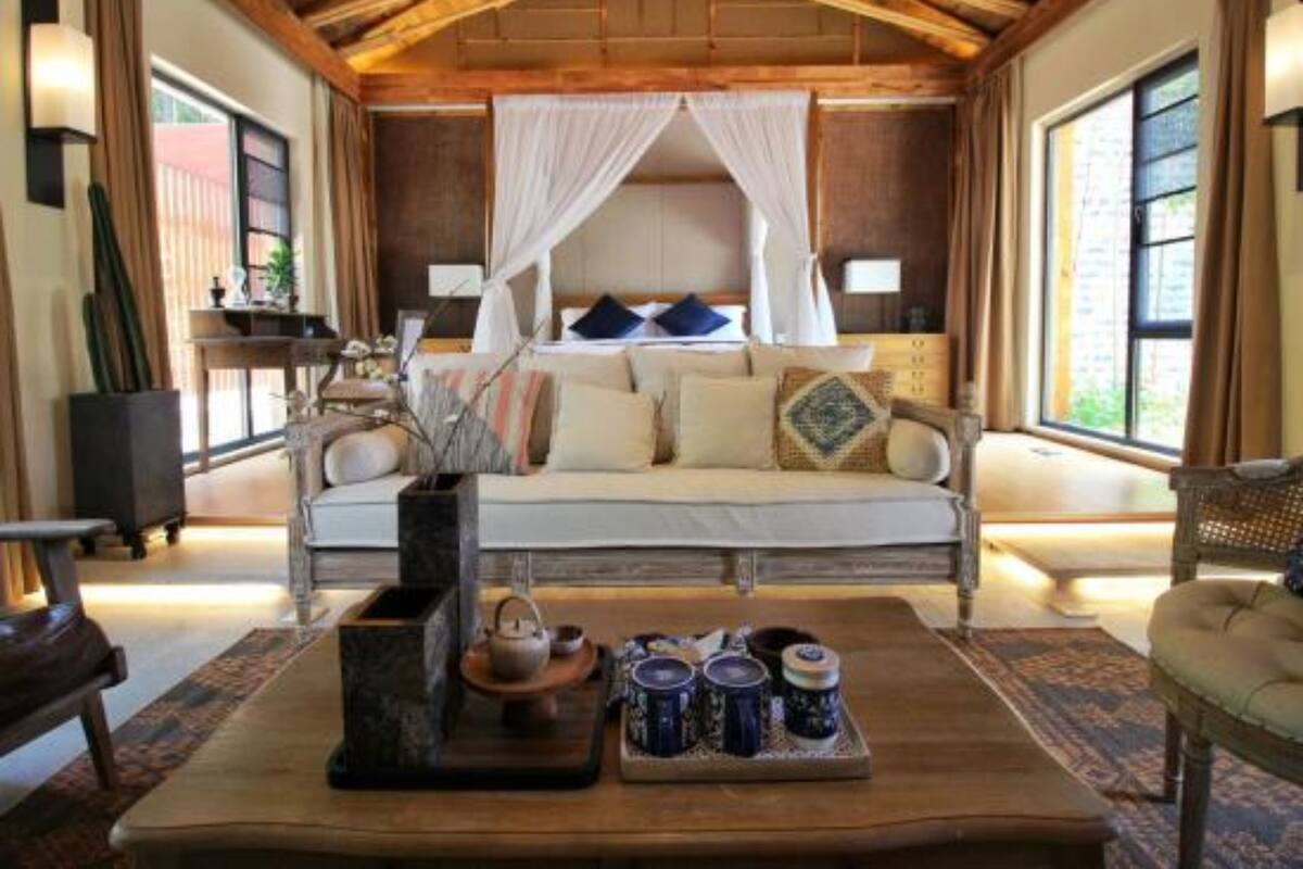 A room with a bed under a canopy, a sofa, a coffee table with tea cups, and a large window.