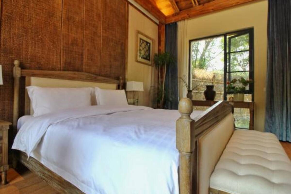 A neatly made bed with white linens in a room with wooden paneling and a large window.