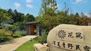 A stone sign with Chinese characters, a pathway leading to a building, and surrounding greenery.