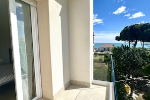 A balcony with a clear view of the sea, a building with a red roof, and a tree. - M026 - Marcelli, new three-room apartment with terrace 80 meters from the sea (Marcelli)