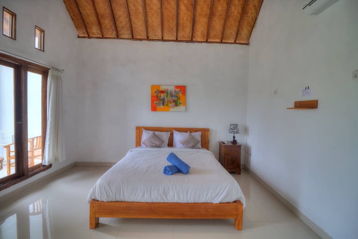 Un dormitorio con cama de madera, ropa de cama blanca, una obra de arte colorida en la pared y una mesita de noche de madera.