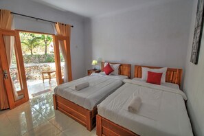 Ein Hotelzimmer mit zwei Betten, einem hölzernen Kopfteil, einem kleinen Tisch und Blick ins Freie durch eine Glastür.