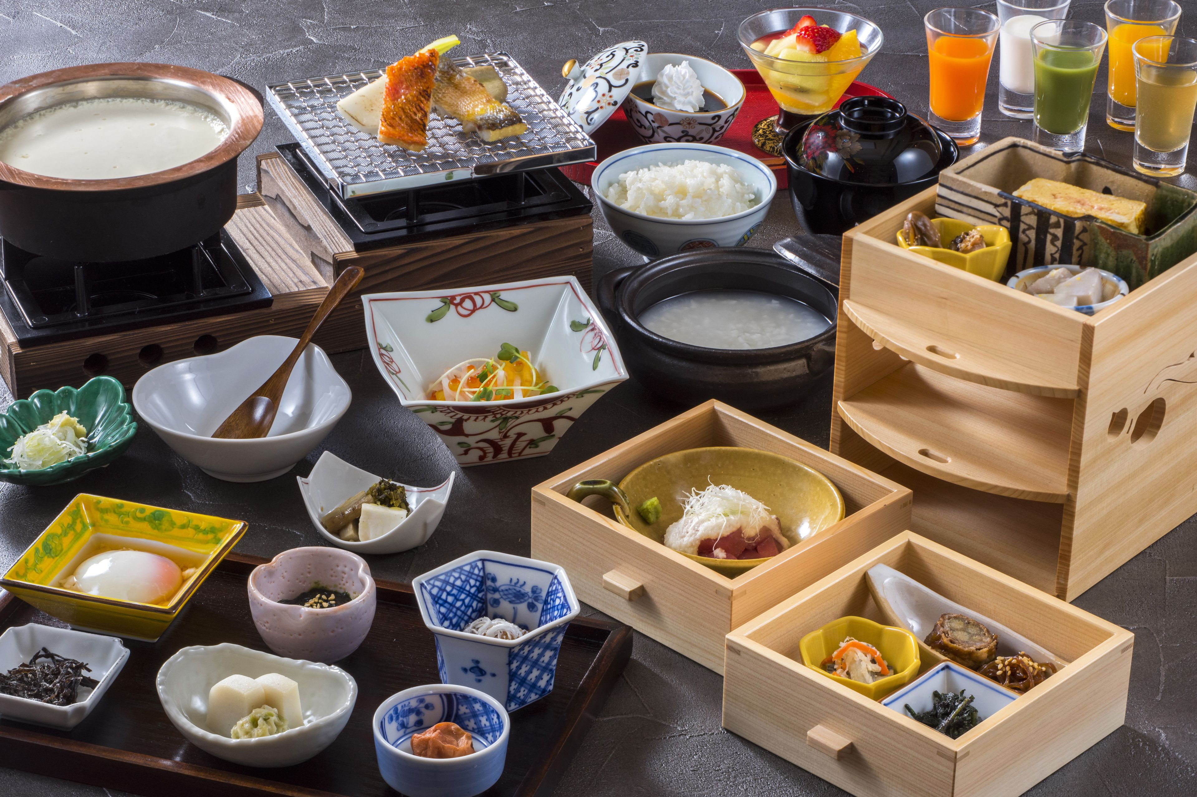 A variety of Japanese dishes and beverages on a table, including a hot pot, rice, soup, and several small bowls with different ingredients.