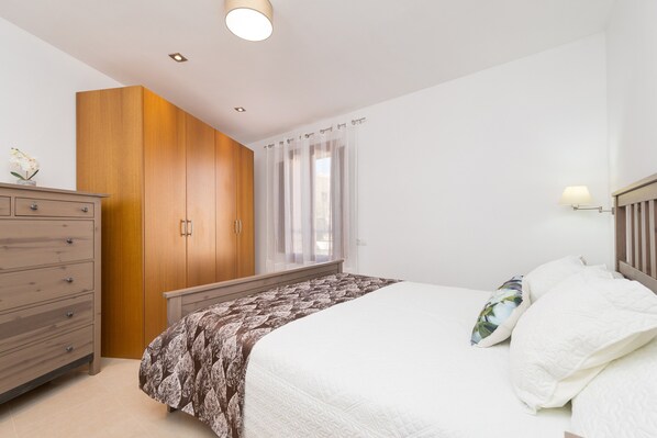 A bedroom with a bed, a wooden wardrobe, a nightstand, and a window with curtains.