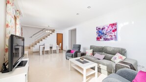 A modern living room with a sofa, coffee table, and a flat-screen TV on a white cabinet. A staircase leads to an upper floor. - BIALI - Chalet with terrace in Buger. Free WiFi (Búger)