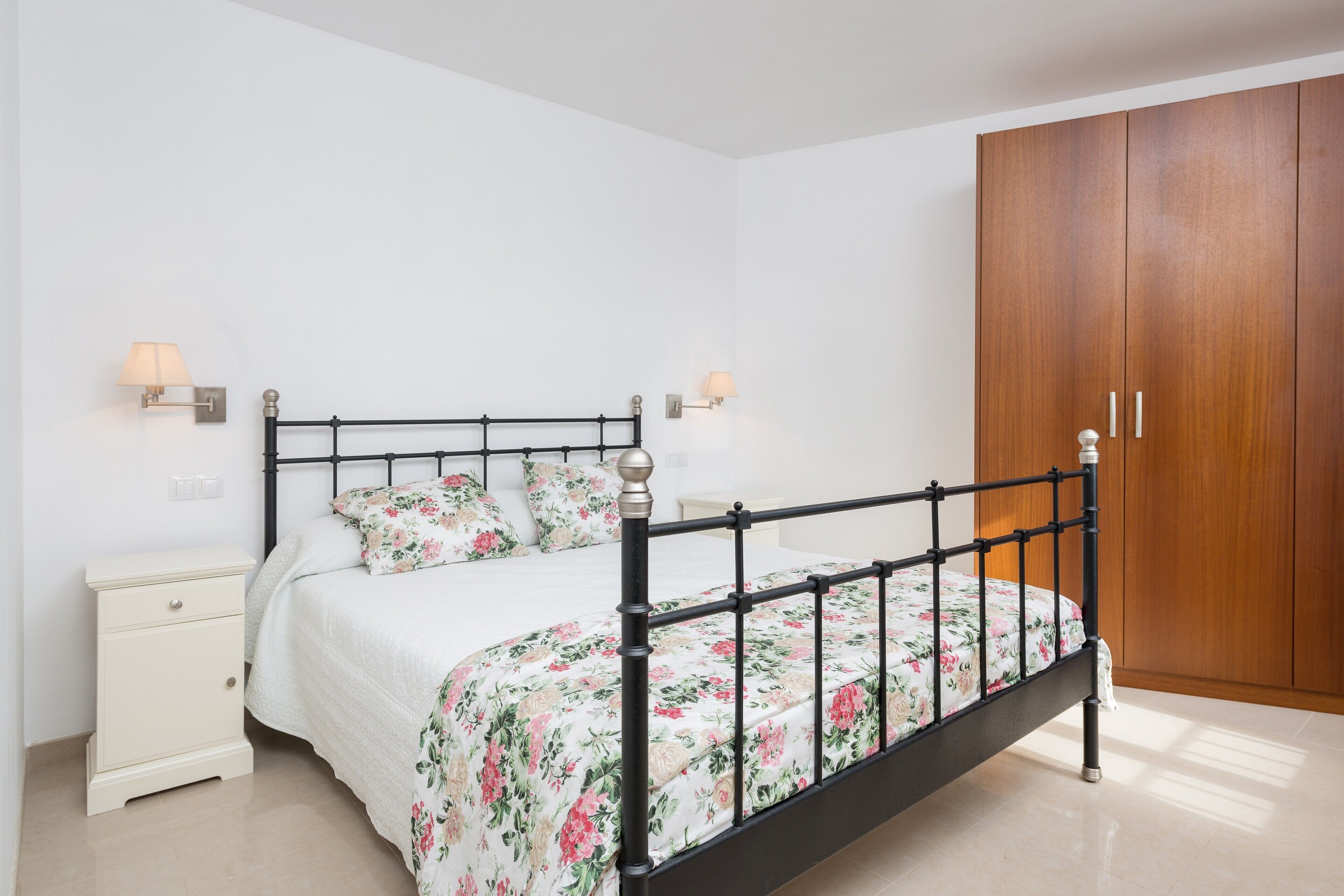 Ein Schlafzimmer mit schwarzem Metallbettgestell, weißer Bettwäsche, einem Holzschrank und zwei Nachttischlampen.