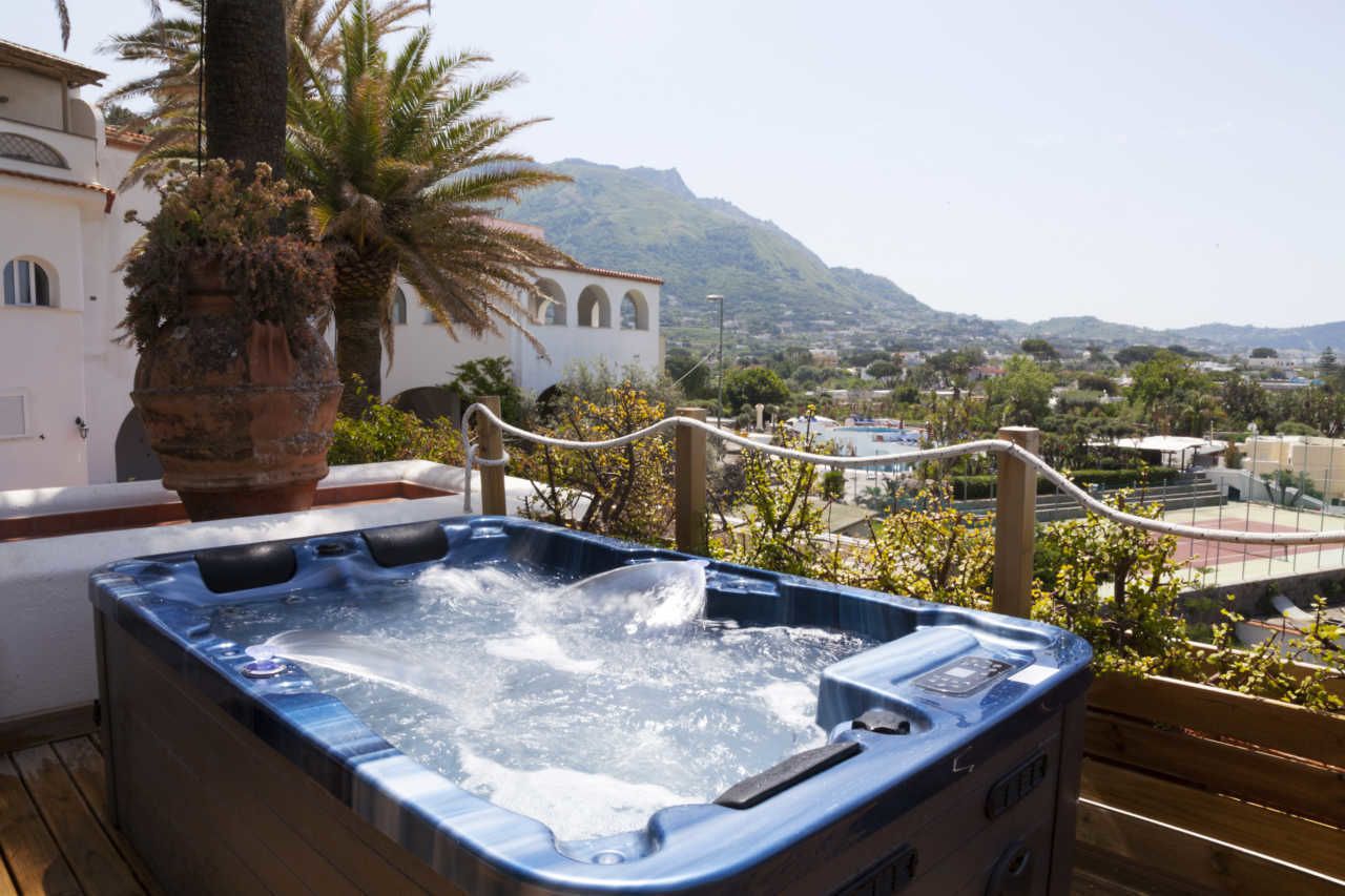 A hot tub on a wooden deck with a view of a town and mountains in the background.