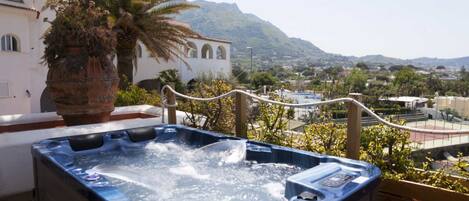 A hot tub on a wooden deck with a view of a town and mountains in the background.