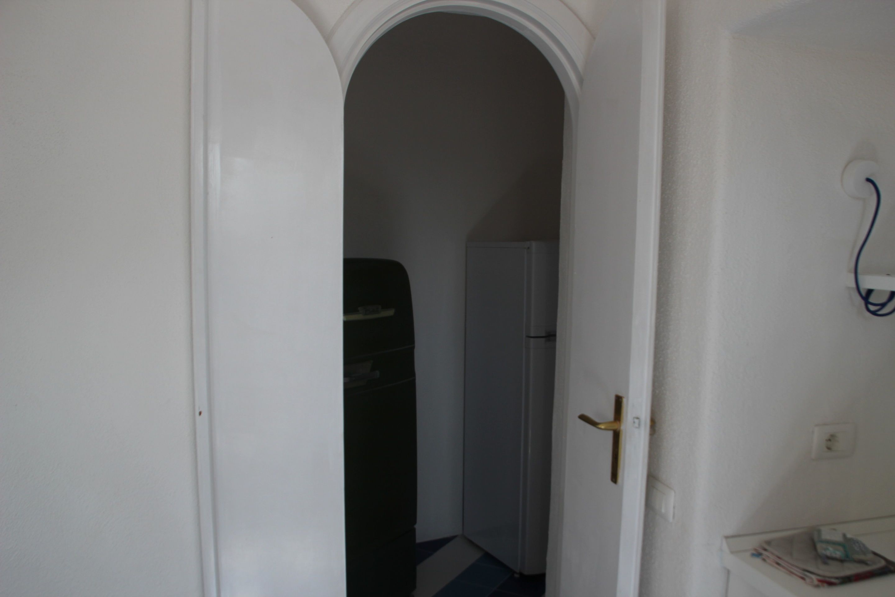 A narrow hallway with a white door on the left, a black door in the center, and a white door on the right. There is a small table with a magazine on the right side.