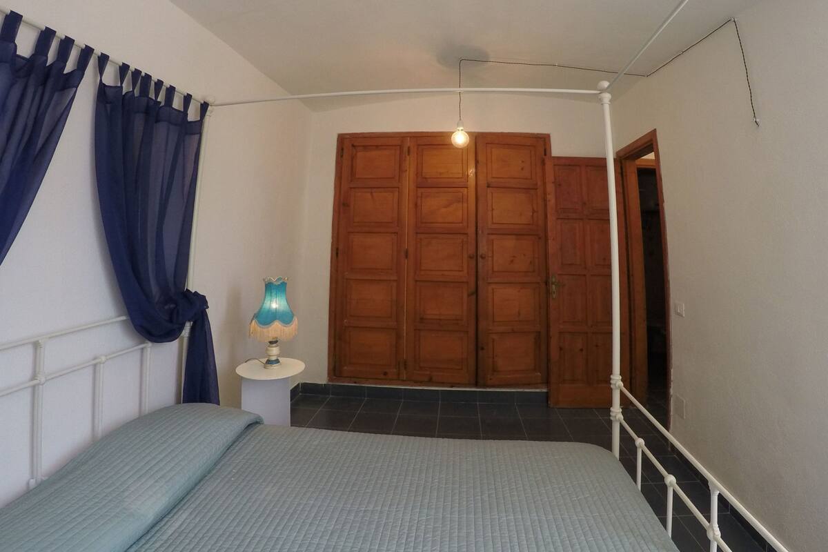 A bedroom with a bed, a nightstand, a lamp, and a wooden wardrobe.